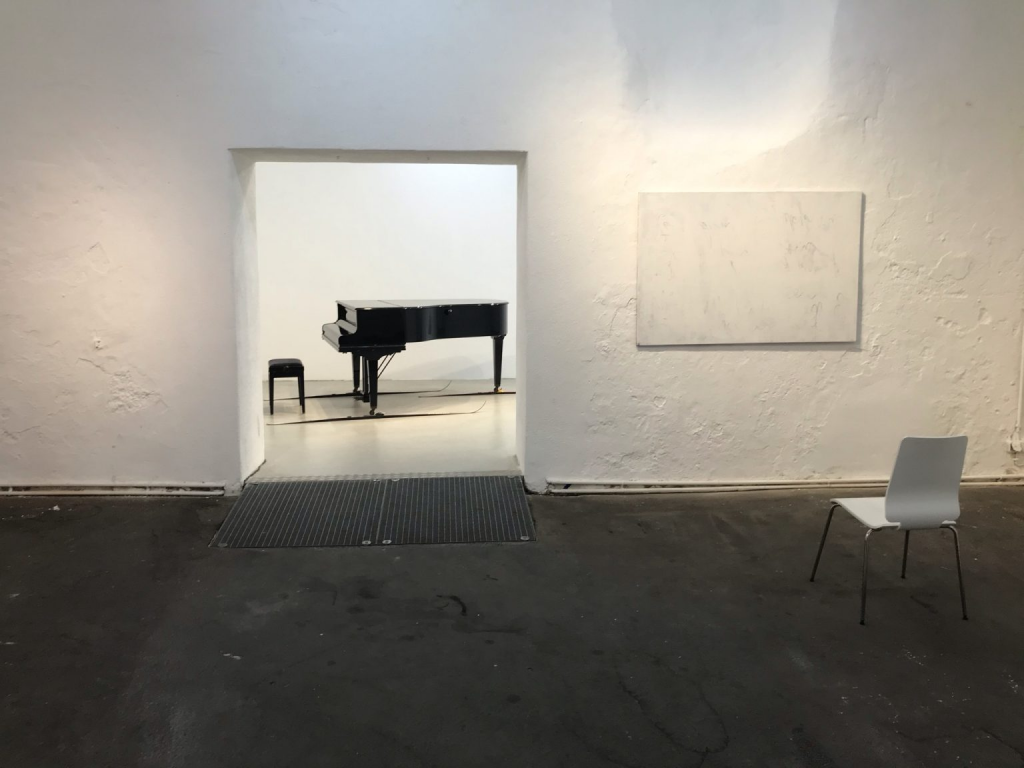 you see a piano on skies and a white canvass with a white chair in front in an exclusive gallery setting